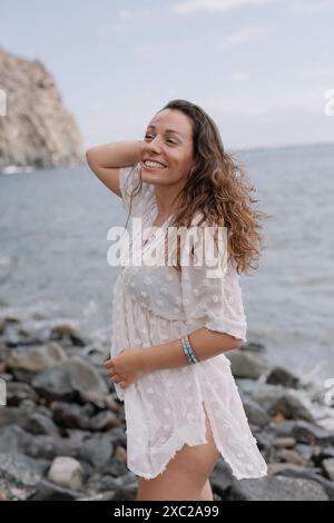Une femme se tient debout sur une plage rocheuse portant une robe blanche Banque D'Images