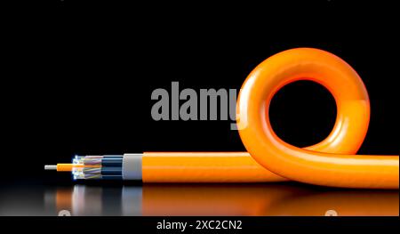 Câble à fibre optique orange reposant sur une surface réfléchissante noire avec une boucle Banque D'Images