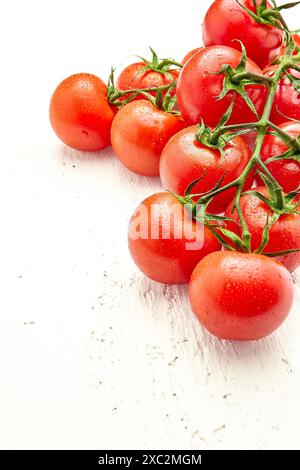Tomates cerises mûres avec des gouttes d'eau sur une surface en bois blanc dans le coin supérieur droit de la photo. Orientation verticale de la photo. Gros plan de Banque D'Images