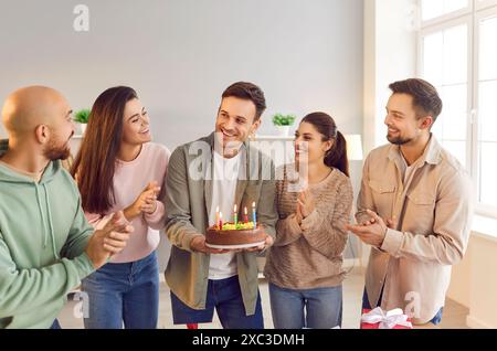 Homme heureux tenant le gâteau debout avec des amis le félicitant avec une fête d'anniversaire à la maison Banque D'Images