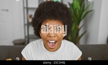 Femme afro-américaine excitée avec les cheveux bouclés portant un t-shirt blanc à l'intérieur. Banque D'Images
