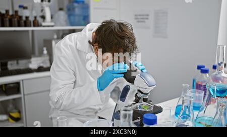 Scientifique spécialisé examinant des échantillons au microscope dans un laboratoire, entouré de verrerie et d'équipement. Banque D'Images