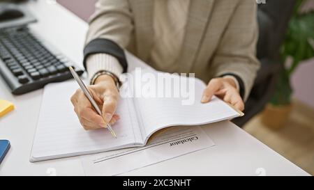 Une femme d'âge moyen écrit dans un planificateur à son bureau, mettant en valeur l'organisation et le professionnalisme. Banque D'Images