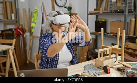 Femme mature utilise un casque vr dans un atelier de menuiserie entouré d'outils et de boiseries. Banque D'Images