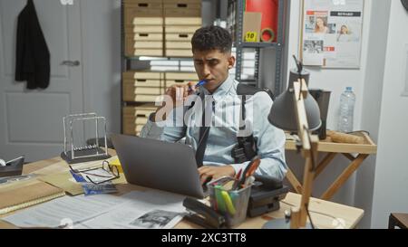 Un homme réfléchi dans le bureau d'un détective immergé dans l'enquête par un ordinateur portable, entouré de dossiers et de preuves. Banque D'Images