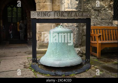 Une grande cloche d'église en laiton avec un panneau indiquant «anneau pour la paix» à l'extérieur de l'église médiévale de la Sainte Trinité à Goodramgate, York, North Yorkshire, Royaume-Uni Banque D'Images