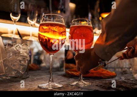 BarTender prépare deux verres de cocktail Aperol spritz sur le comptoir du bar, ajoute des tranches d'orange fraîches. Boisson italienne alcoolisée typique, apéritif fait avec Banque D'Images