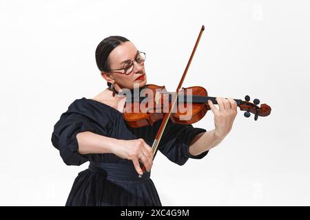 Des mélodies gracieuses. Portrait de femme élégante en robe noire jouant du violon, appréciant la performance solo isolée sur fond blanc Banque D'Images