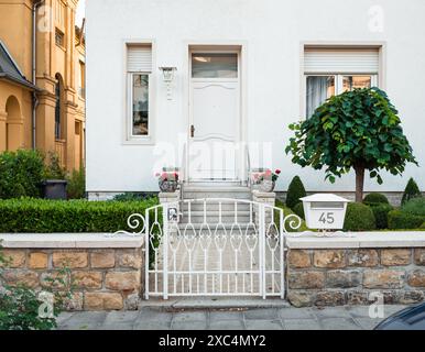 Belle maison blanche avec porte blanche, pots de fleurs et arbustes le long du chemin étroit menant à l'entrée. Petite clôture en pierre avec portail en métal. Banque D'Images