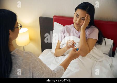 Femme malade recevant un appareil de mesure de la température de son parent dans la chambre Banque D'Images