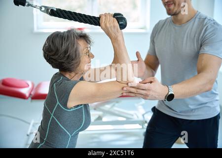 L'employé de la clinique de fitness aide un retraité à effectuer des exercices de réadaptation Banque D'Images