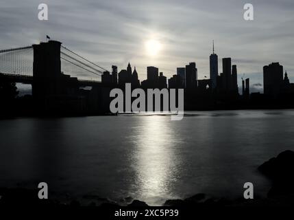 coucher de soleil derrière la silhouette de new york city downtown skyline avec pont de brooklyn (longue exposition) gratte-ciel noir foncé avec une lumière vive dans le ciel d Banque D'Images