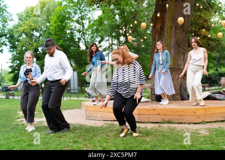 Soirée dansante joyeuse en plein air, avec des individus de différents âges profitant de l'ambiance festive sous des jeux de lumières illuminés. Ils dansent Banque D'Images