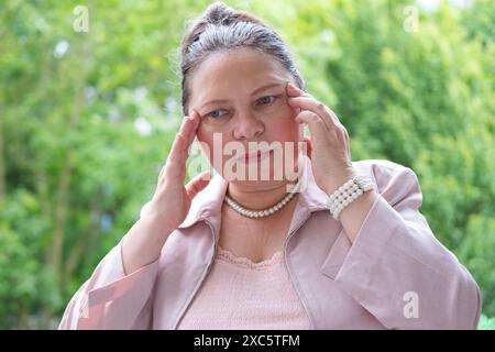 close-up charismatique femme d'affaires mature avec des maux de tête de migraine sévères accroche la tête dans la douleur, l'inconfort sévère, l'interruption du travail, la douleur chronique Banque D'Images