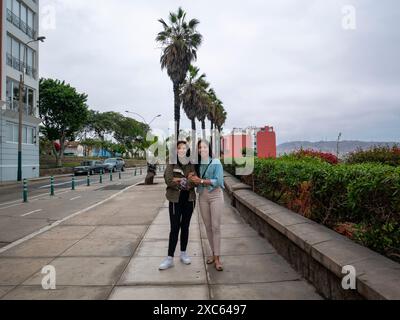 Lima, Pérou - juillet 30 2023 : deux sœurs posent à la caméra dans une rue avec des palmiers et d'autres arbres un jour nuageux Banque D'Images