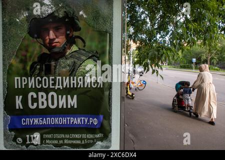 Moscou, Russie. 14 juin 2024. Une femme se tient à un arrêt de bus à côté d'une publicité pour la conscription militaire, montrant un soldat russe avec une inscription indiquant «Join to Yours», à Moscou, en Russie Banque D'Images
