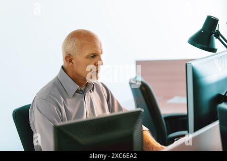 Spécialiste informatique mature axé sur le codage sur un ordinateur de bureau dans une salle de serveurs entourée de technologie Banque D'Images
