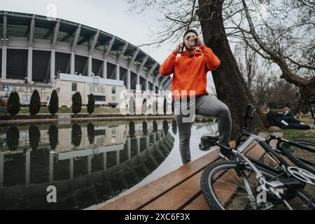 Jeune homme prenant une pause de vélo dans un parc nuageux avec un vélo au premier plan Banque D'Images