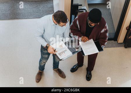 Vue aérienne d'un coéquipier multiracial discutant de graphiques et de graphiques avec un collègue plus jeune tenant une tablette numérique. Banque D'Images