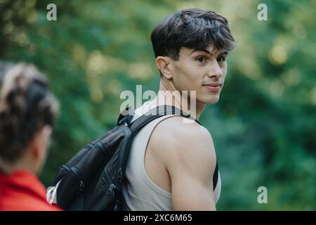 Jeune homme avec sac à dos regardant en arrière lors d'une randonnée dans une forêt Banque D'Images