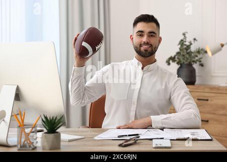 Jeune homme avec ballon de football américain à table dans le bureau Banque D'Images