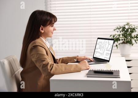 Femme travaillant avec la carte cadastrale sur ordinateur portable à table dans le bureau Banque D'Images