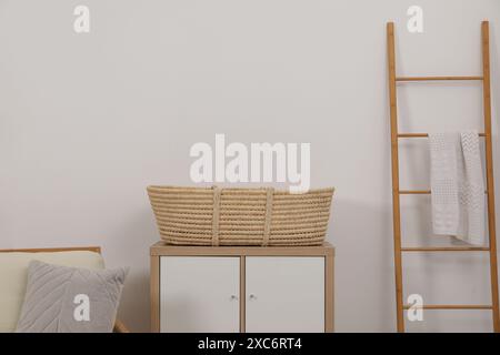 Fauteuil avec coussin, panier en osier sur table de chevet et échelle en bois dans la chambre Banque D'Images