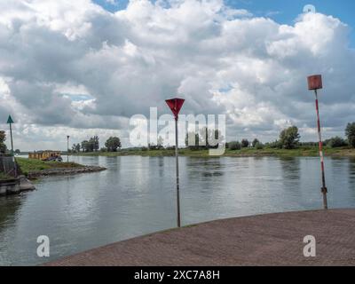 Un vieux mur de briques recouvert de mousse jaune sur la rive d'une rivière, bateaux en arrière-plan sous un ciel nuageux, zutphen, gueldre, pays-bas Banque D'Images