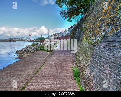 Une rivière avec de grosses pierres sur la rive, un bateau passe, et en arrière-plan un pont sous un ciel nuageux, zutphen, gueldre, pays-bas Banque D'Images