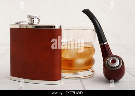 Nouveau flacon de hanche, verre de whisky froid et pipe à fumer sur table Banque D'Images