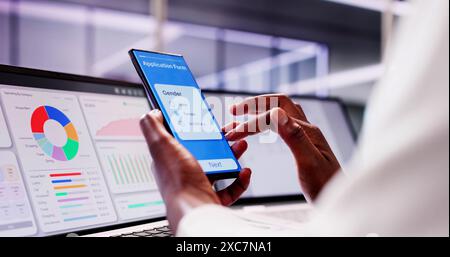 African American Student remplit la demande de bourse en ligne en utilisant un téléphone noir et un ordinateur portable intelligent au bureau du Collège Banque D'Images