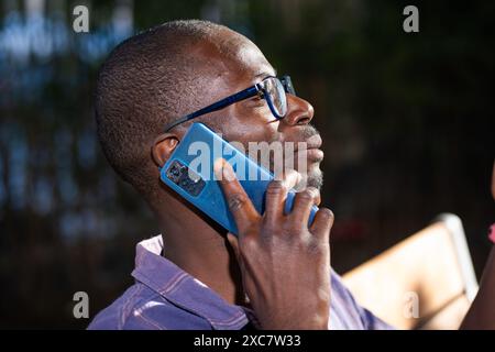 Gros plan d'un jeune homme afro-américain portant des lunettes, parlant sur un smartphone à l'extérieur - conversation téléphonique décontractée - atmosphère concentrée et détendue Banque D'Images