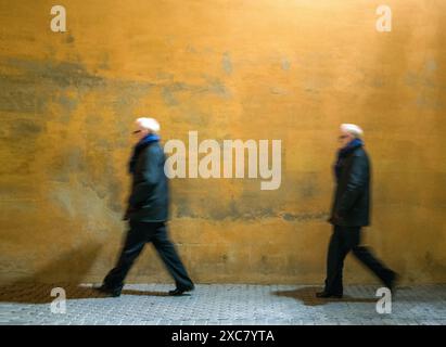 Homme se poursuivant devant un mur jaune vibrant à Séville, España. Capture le mouvement et l'énergie de la vie urbaine. Banque D'Images