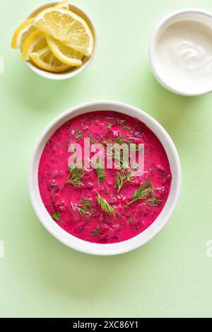 Délicieuse soupe froide de betterave d'été dans un bol blanc sur fond vert. Concept sain de détox ou de nourriture végétarienne. Vue de dessus, pose à plat Banque D'Images