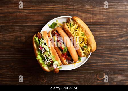 Hot-dogs chargés de garnitures assorties sur fond de bois. Vue de dessus, pose à plat Banque D'Images