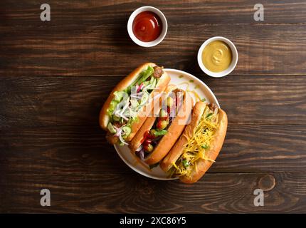 Hot-dogs chargés de garnitures assorties sur fond de bois. Vue de dessus, pose à plat Banque D'Images