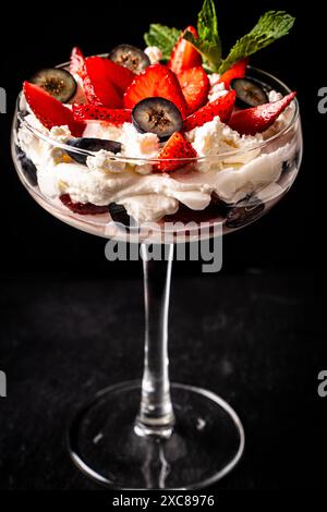 Dessert aux fraises dans un grand verre. Fraises et bleuets avec mascorpone et menthe sur fond noir. Gros plan. Foyer sélectionné. Photo de haute qualité Banque D'Images