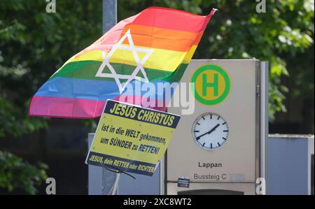 Oldenburg, Allemagne. 15 juin 2024. Un participant au 30ème Christopher Street Day à Oldenburg tient de manière démonstrative un drapeau arc-en-ciel derrière un panneau indiquant «Jésus Christ est venu au monde pour sauver les pécheurs!» tenu par une personne au bord de la route pendant le défilé à travers le centre-ville. La devise de la CDD de cette année à Oldenburg est "sur les barricades pour les droits de l'homme queer!". Crédit : Focke Strangmann/dpa/Alamy Live News Banque D'Images