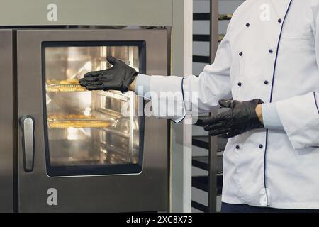 A la boulangerie : baker debout près d'un four électrique. Industrie alimentaire Banque D'Images