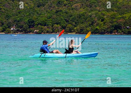 Couple caucasien ramant un kayak dans les eaux claires de la baie de Loh Dalum sur la rive nord de l'île de Koh Phi Phi dans la mer d'Andaman, province de K Banque D'Images