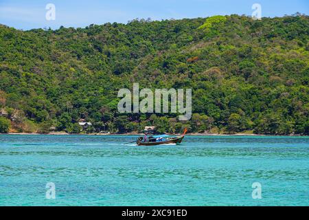 Bateau à longue queue naviguant dans les eaux claires de la baie de Loh Dalum sur la rive nord de l'île de Koh Phi Phi dans la mer d'Andaman, province de Krabi, T. Banque D'Images