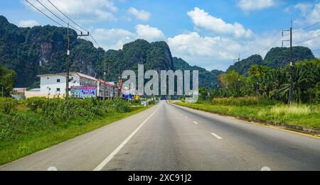 Route droite passant par une jungle luxuriante entourée de falaises karstiques calcaires en Asie du Sud-est (Thaïlande, entre Krabi, Phang Nga et Phuket) Banque D'Images