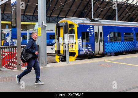 Un passager masculin marchant sur la plate-forme a passé le sprinter express de classe 158 appartenant à Scotrail, le train régional de passagers diesel à unités multiples (DMU) à qu Banque D'Images