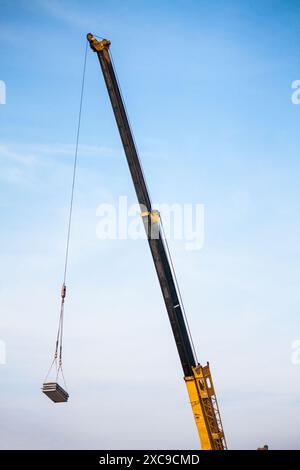 bras télescopiques jaunes de camion de grue de construction mobile soulevant la dalle de béton à la maison de construction au chantier de construction Banque D'Images