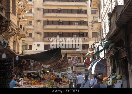 Le Caire, Égypte. 14 juin 2024 le bâtiment art-déco Grand Hôtel à Al Azbakeya, centre-ville du Caire vu du souk Al Tawfik un fruit et légume populaire m Banque D'Images