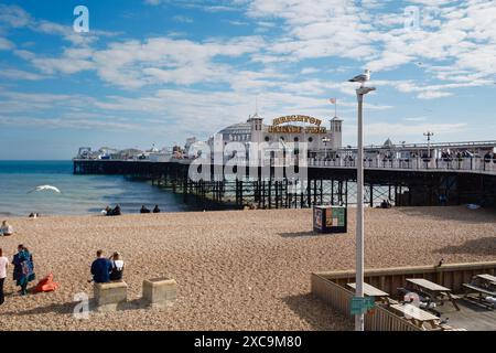 Brighton Palace Pier et une vue sur la plage tranquille par une froide journée d'été avec mouette perchée sur un lampadaire et une dispersion de gens assis Banque D'Images