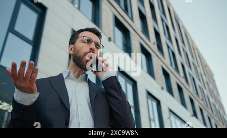Insatisfait émotif homme d'affaires masculin homme d'affaires caucasien adulte homme d'affaires a choqué l'employé de bureau d'entrepreneur d'employeur parlant téléphone mobile à l'extérieur incroyable Banque D'Images