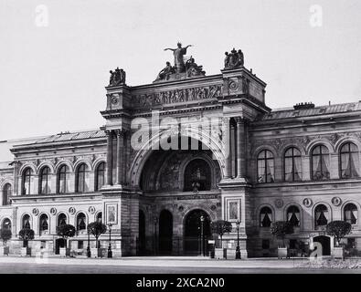 Photographie en noir et blanc prise par Achille Quinet en 1870, montrant la grande entrée du Palais de lIndustrie à Paris, France. L'image met en valeur l'architecture ornée et les détails complexes du bâtiment, y compris son imposante arche, ses sculptures décoratives et ses nombreuses fenêtres. Banque D'Images