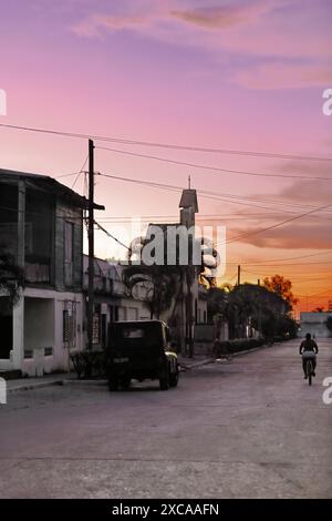 389 le coucher de soleil sur la rue Calle 2 de Diciembre tourne le ciel et l'ambiance urbaine rougeâtre, avec les gens rentrant à la maison pour la nuit. Niquero-Cuba. Banque D'Images