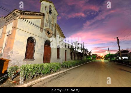 394 le coucher de soleil sur Calle 2 de Diciembre Street et l'église Iglesia San Francisco Javier transforme l'atmosphère urbaine rosée-violacée. Niquero-Cuba. Banque D'Images